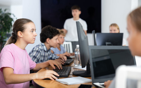 Portrait of teen schoolgirl sitting at table in computer class during lesson, smiling at camera....