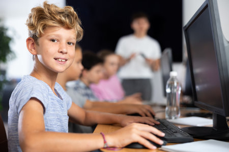 Smiling preteen boy sitting at computer table in training roomの写真素材