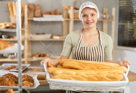 Portrait of female baker holding a basket of baguettes and fresh bread in handsの写真素材