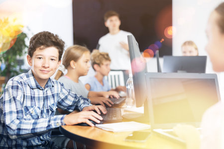 Smiling preteen boy sitting at computer table in training room