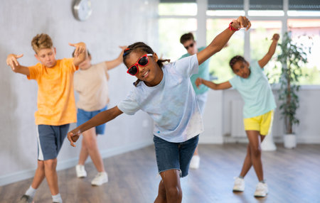 Positive juvenile boy engaged in Breakdancing in training room with childrens group