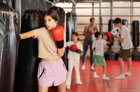 Teen girl in boxing gloves hits punching bag in gymの写真素材