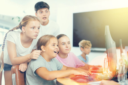 Preteen boys and girls working on computer together with teacher in IT cabinet
