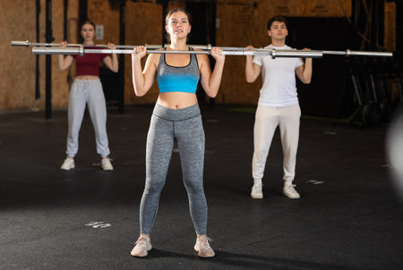 Slender girl trains muscles of arms and back using barbell and differentiated weighting in gym