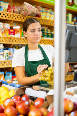 Female shopping assistant weighing grapes in grocery shopの写真素材