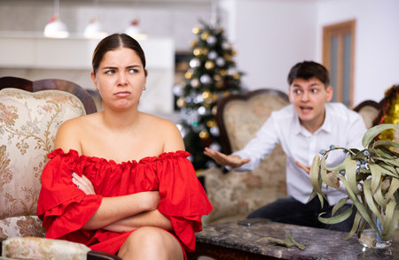Disappointed young couple arguing among themselves before Christmas Eve while sitting on sofa in living room at homeの写真素材