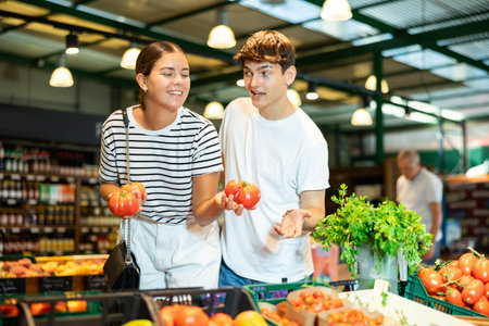 Young woman and young guy choose tomatoes in grocery storeの写真素材