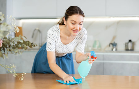 Positive middle-aged woman cleaning the surface of kitchen table