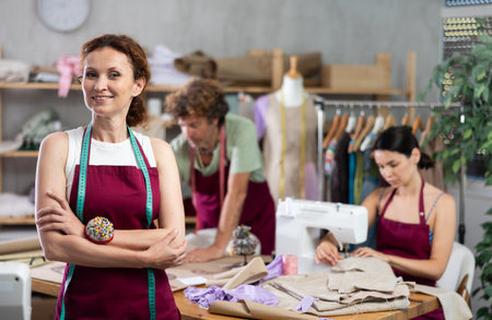 Middle-aged female dressmaker inviting clients while others sew and drawの写真素材