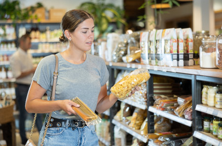 Girl comparing different types of pasta in organic food storeの写真素材