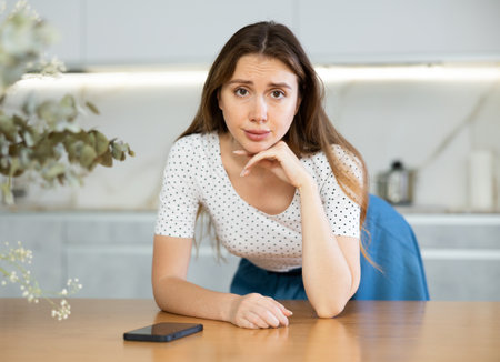 Upset young girl leaned on table and looks at smartphone screen, received unpleasant news, smsの写真素材