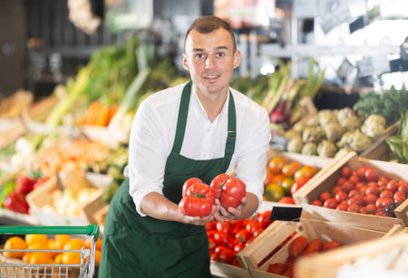 Man supermarket worker with some tomatoes in hands examines productの写真素材