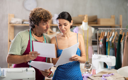 Male tailor shows paper sketch of dress to woman client,の写真素材