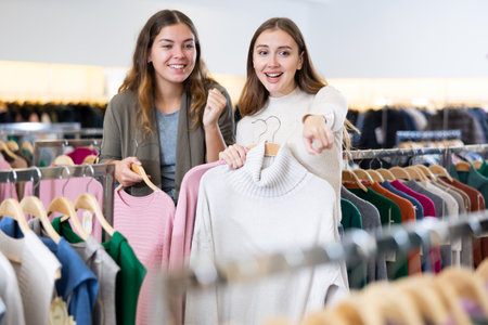 Excited young women holding warm clothes on racks and enjoying shopping together in a boutiqueの写真素材