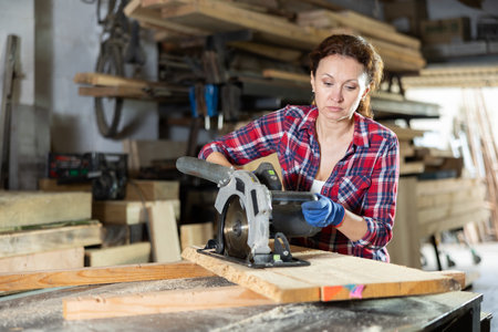 Working at sawmill - woman saws wooden board using circular sawの写真素材