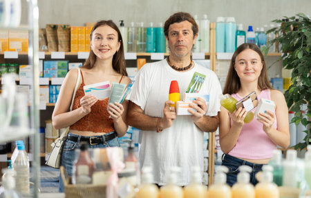 Father, mother and daughter choose different products together in modern pharmacyの写真素材