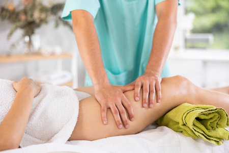 Masseur doing thigh massage to adult womanの写真素材