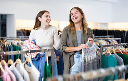 Excited young women holding jumpers with a graphic pattern while shopping in a shopping mallの写真素材