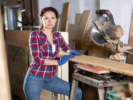 Female employee of workshop cuts wooden board into narrow parts using circular sawの写真素材