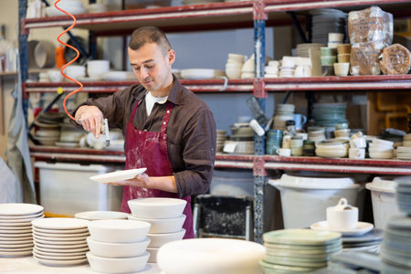 Artisan dusting off ceramic wares with air blow gun in pottery workshopの写真素材