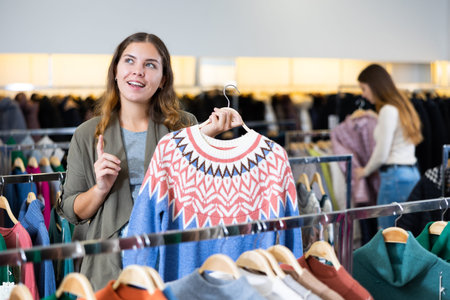 Young woman choosing knitted sweater in store