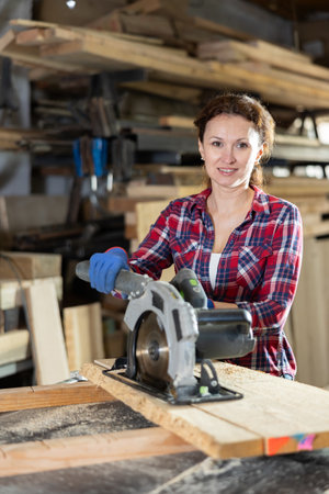 Working at sawmill - woman saws wooden board using circular sawの写真素材