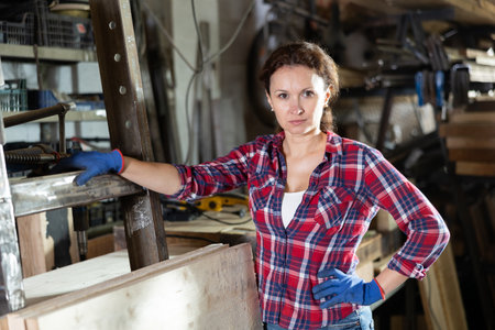 Female employee of workshop stands next to iron rails of workpieces, measures lengthの写真素材