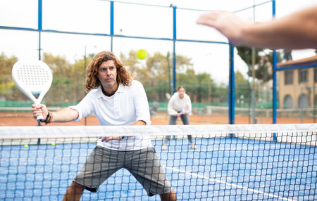 Portrait of middle-aged Latin male in sportswear enjoying popular sport padel game on tennis court outsideの写真素材