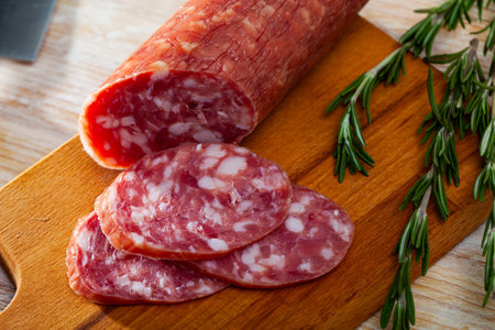 Thin salchichon sausage slices on wooden background, view from above