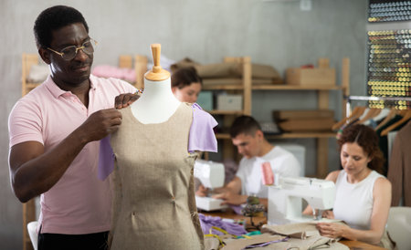 African man student works with mannequin, others pupils sewing, working in backgroundの写真素材