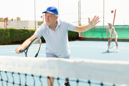 Man with black racket playing match in open behind net court outdoors.の写真素材