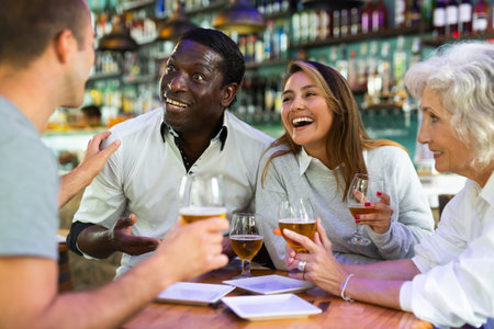 Happy friends cheering and drinking beer at in pub indoor. Main focus right in center