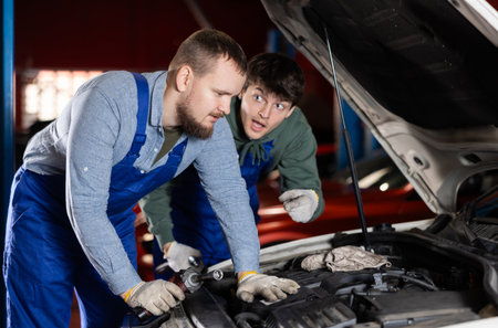 Two auto mechanics work together to diagnose an engine under the hood of a car in repair shopの写真素材