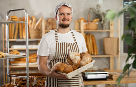 In sales area room of bakery, there is guy with loaf breads and baguetttes in wicker basket in handsの写真素材