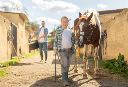 Happy boy leads a horse by the bridle for a walk in pastureの写真素材