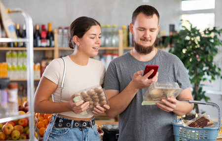 Spouses inspects oyster mushrooms and champignons, photographs QR code on label by smartphoneの写真素材
