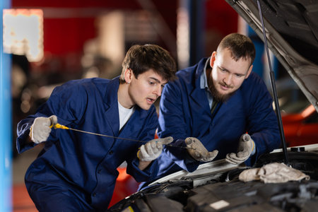 Two auto mechanics checking engine oil level under the hood of car together in garageの写真素材