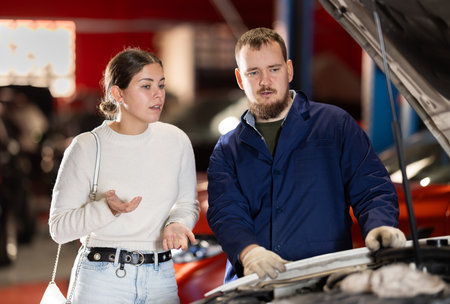Mechanic checking young woman client car in car service centerの写真素材