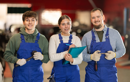 Team of auto mechanics, two men and one woman, wearing blue overalls and posing, ready to provide professional vehicle serviceの写真素材