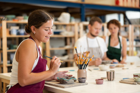 During workshop at master class, female employee paints clay vessel plate