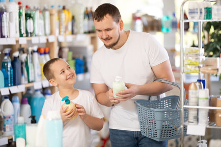 Schoolboy son and dad are choosing liquid hand soap in storeの写真素材