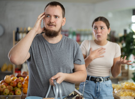 Wife stands behind husband and yells at companion in shopの写真素材