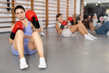 Girls in boxing gloves are sitting on floor, doing abdominal exercise and working with handsの写真素材