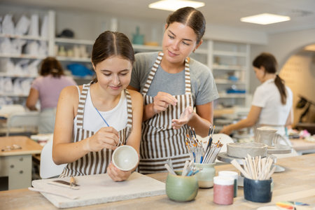 Female teacher teaches girl how to paint ceramic cupの写真素材