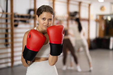 Girl coach in boxing gloves is standing in gym