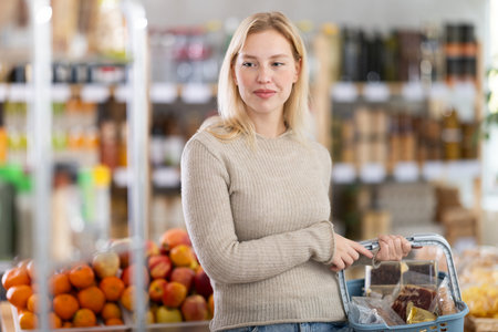 Portrait of girl shopper with a shopping cart choosing some products in supermarketの写真素材