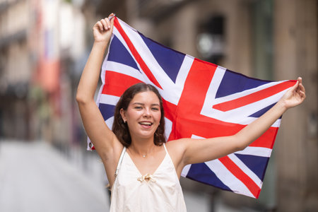 Cheerful girl holding national flag of UK flag, standing outdoorsの写真素材