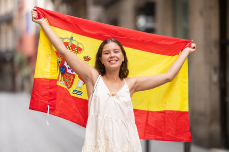 Patriotic young woman waving the flag of Spain on city streetの写真素材