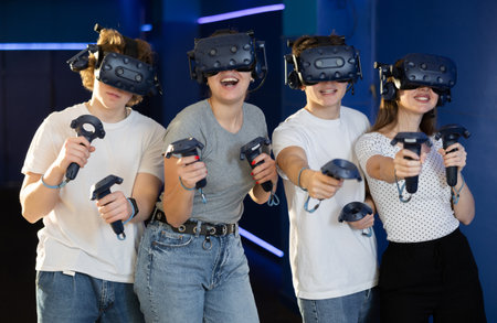group of four friends wearing virtual reality glasses and with joysticks are playing dynamic gameの写真素材
