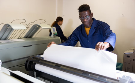 Printing house employee works on printing equipmentの写真素材